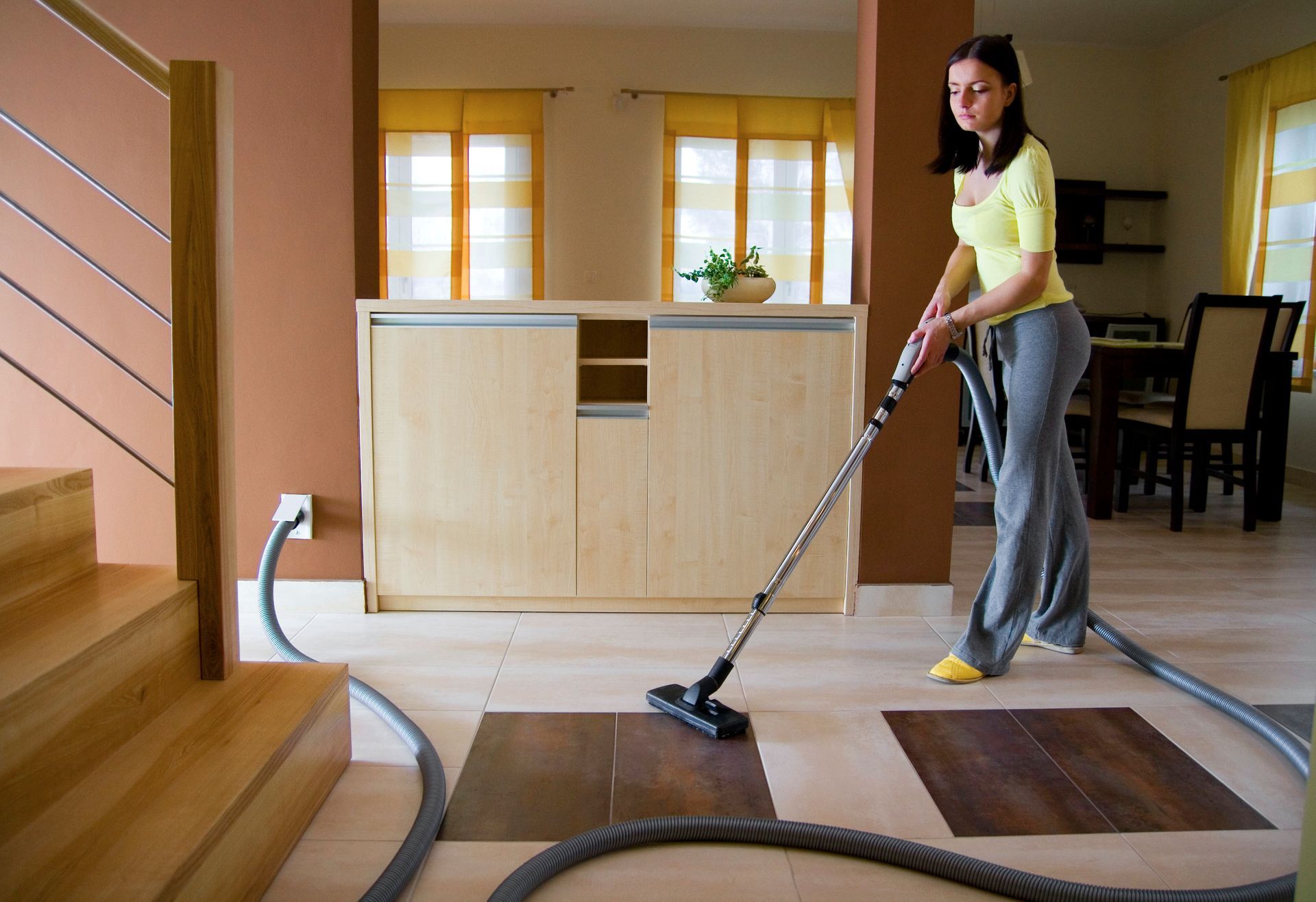 Image of a woman using an attachment to her central vacuum system.