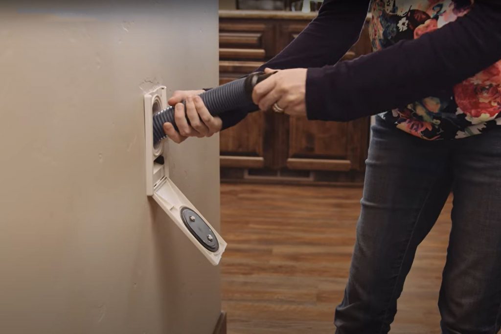 A person's hands pulling a central vacuum hose from the wall valve in order to clean their home.