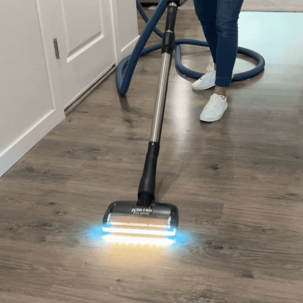 Woman using a central vacuum system on a hardwood floor.