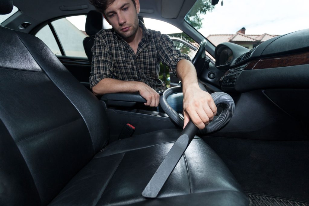 Detailer vacuuming a car's driver seat with a central vacuum hose and crevice tool