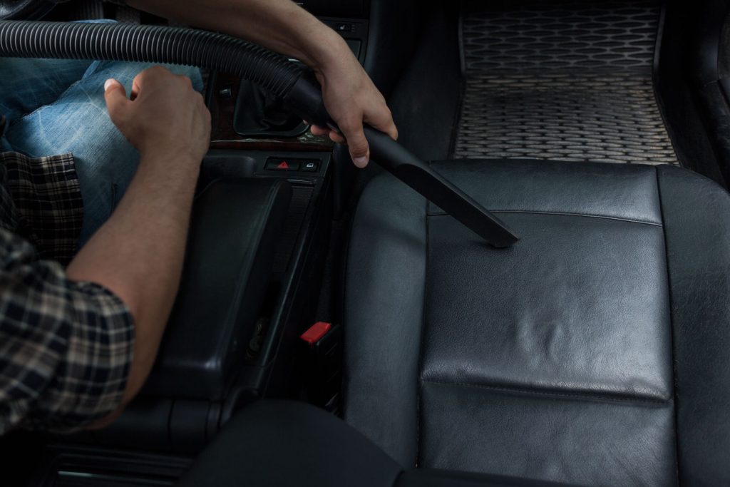 Close-up of a vacuum hose and crevice tool cleaning a black leather car seat