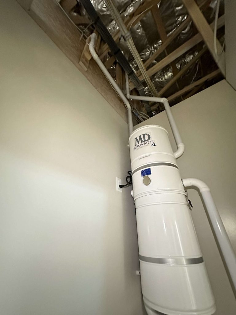 MD AirMaster XL central vacuum power unit in a utility closet, with piping routed up through the ceiling.