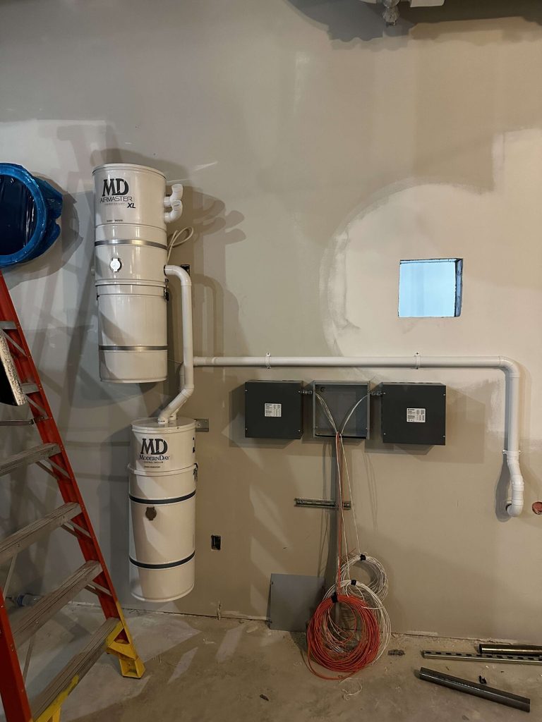 Two MD central vacuum power units with white piping and control panels mounted on a wall during a commercial installation.