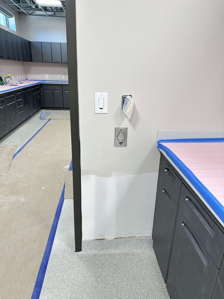 Stainless steel central vacuum inlet on a wall beside clinic treatment-area cabinetry.