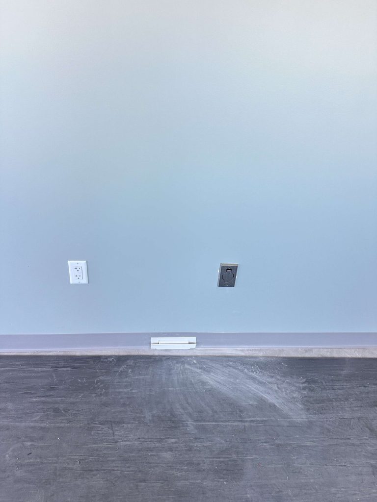 Stainless steel central vacuum wall inlet and a white baseboard sweep inlet in a finished commercial room.